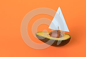 Half of fresh avocado fruit - yacht or sailboat with sail on orange background