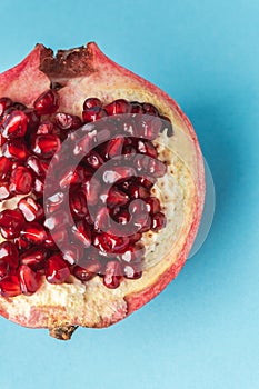 Half of fresh pomegranate fruit on blue pastel background. Ripe pomegranate cracked in a half with red juicy seeds exposed