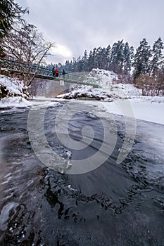 Half-frozen Hornad river with rapids in winter at sunset Slovak Paradise. An iron bridge over a frozen river.