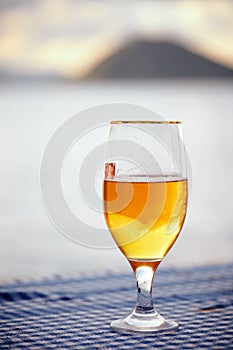 Half full glass of  beer on the table with blurred sea, sky and island background