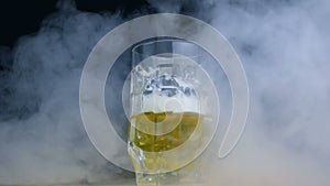 Half full glass of pilsener or lager beer spinning in smoke in slow motion