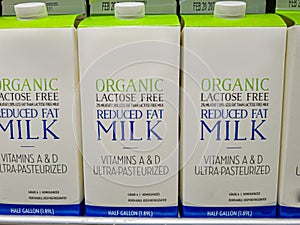 Half gallon cartons of lactose free reduced fat organic milk on fridge shelf.