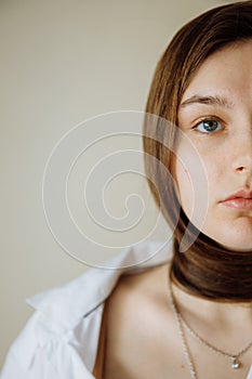 Half of the girl`s face. She has delicate features. The girls dark hair is wrapped around her neck.