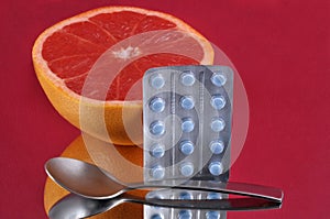 Half grapefruit with a blister pack of medicines on a red background