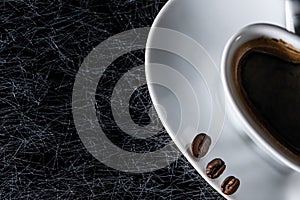 Half of a heart shaped coffee cup with black coffee beans on a black background with silver lining.