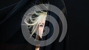 Half hidden portrait of blonde sexy woman fashion model, behind black cloth, whose hair is electrostatic charged and hanging on