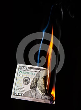 half a hundred dollar bill burning with a bright flame on a black background