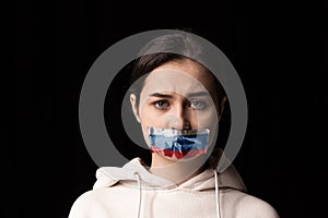 Half-legth portrait of young emotional upset girl with three colors duct tape over her mouth isolated on dark background