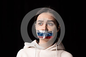 Half-legth portrait of young emotional upset girl with three colors duct tape over her mouth isolated on dark background