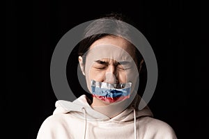 Half-legth portrait of young emotional upset girl with three colors duct tape over her mouth isolated on dark background