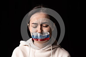 Half-legth portrait of young emotional upset girl with three colors duct tape over her mouth isolated on dark background