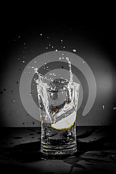 Half Lemon dropped in a glass of water with water splashes with a black to grey background