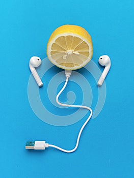 Half a lemon with wireless headphones and USB cable on a blue background