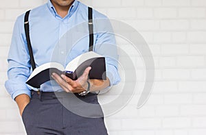 Half-length,Close up Man in blue shirt holding black book of the Bible, Buddhist, Catholic, Christian, prayer,on wall background,