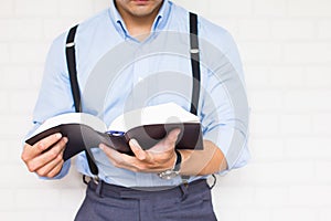 Half-length,Close up Man in blue shirt holding black book of the Bible, Buddhist Catholic Christian prayer on wall background,