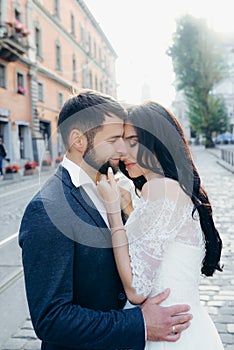 Half-length portrait of the beautiful loving newlywed couple hugging. The pretty brunette bride is gently stroking the