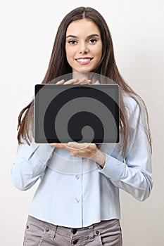 Half-length portrait of brunette young smiling woman showing blank tablet screen to camera isolated on white background