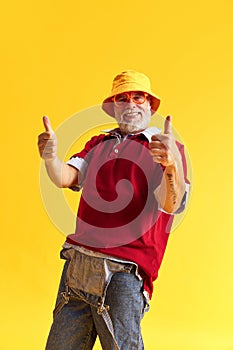 Half-length portrait of happy satisfied senior man showing thumb up. Beard and denim, jeans suit, red t-shirt, glasses