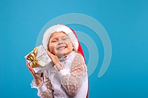 Half length portrait of a little smiling blonde girl  with Sante Claus`s cap holding a gift box