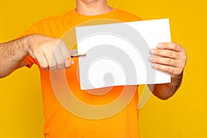 Half-length portrait of a man holding a blank sheet with a hole-punching device,  on yellow studio background.