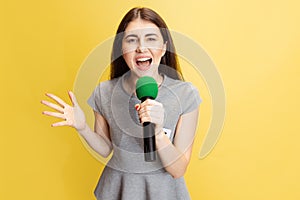 Half-length portrait of young girl, correspondent holding reporter microphone isolated on yellow studio background