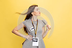 Half-length portrait of young girl, correspondent holding reporter microphone isolated on yellow studio background