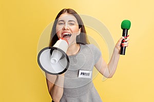 Half-length portrait of young girl, correspondent shouting at megaphone isolated on yellow studio background. Concept of