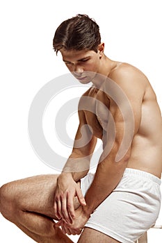 Half length portrait of young, handsome, fit, shirtless man bowed his head and looked down against white studio