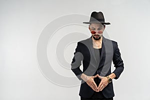 Half length portrait of young handsome serious modern male wearing black suit and hat in round sunglasses