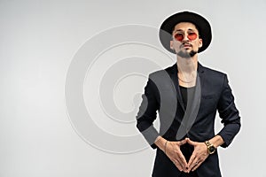 Half length portrait of young handsome serious modern male wearing black suit and hat in round sunglasses