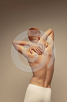 Half-length portrait of young man posing shirtless in underwear isolated over grey studio background. Muscular build