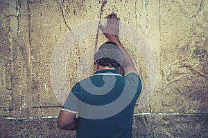 Half-length shot of an old man standing with his hand up and touching the Jewish wailing wall. Pilgrimage in Jerusalem, Israel to