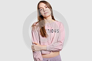 Half length shot of serius contemplative European woman keeps hands partly crossed oves chest, dresed in casual loose sweatshirt, photo