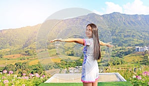 Half length of young Asian woman feeling free with arms wide open at beautiful trees and mountains on blue sky with morning