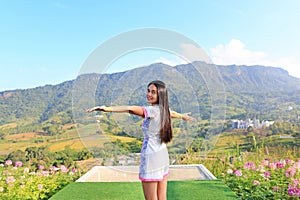 Half length of young Asian woman feeling free with arms wide open at beautiful trees and mountains on blue sky with white puffy