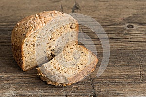 Half a loaf of homemade whole grain bread with various seeds and two slices on a wooden background