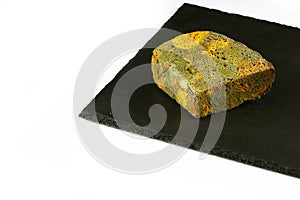 Half a loaf of mouldy rye bread on a black shale board isolated on white background, concept of inedible products, closeup, set