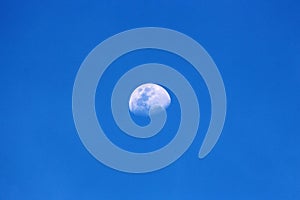 A half moon visible in the afternoon blue sky