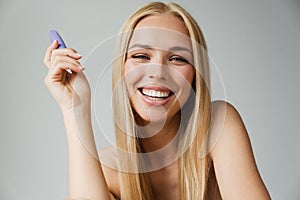 Half-naked blonde woman smiling while holding mascara