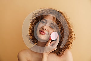 Half-naked ginger woman smiling while showing cosmetic sponge