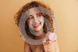 Half-naked ginger woman smiling while showing cosmetic sponge