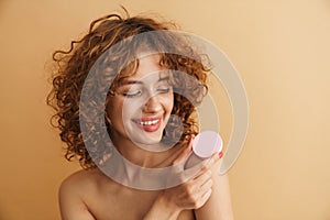 Half-naked ginger woman smiling while showing cosmetic sponge