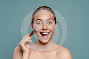 Half-naked ginger woman smiling and using cosmetic brush