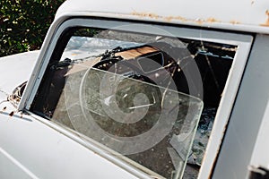 Half-open window of an old abandoned truck with broken glass and spider webs inside.