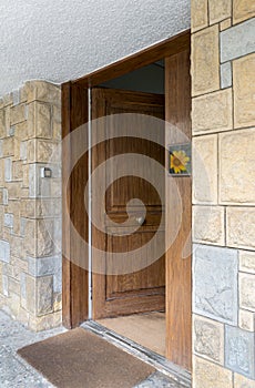 Half opened front wooden door at a stone bricks wall