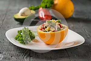 Half an orange with avocado salad and chicken with parsley on a white plate.