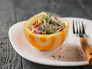 Half orange with chicken and avocado salad with fork on white plate.