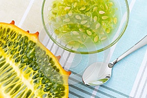 Half of orange kiwano cucumis metuliferus, horned melon, glass bowl with kiwano pulp and a spoon on a tablecloth. Fruits,