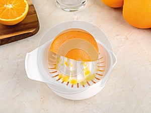 Half an orange on a plastic manual citrus juicer in the process of squeezing juice on a kitchen table. Vegetarian, raw food diet