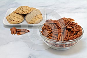 Half pecans in a glass  bowl with pecan cookies in the background